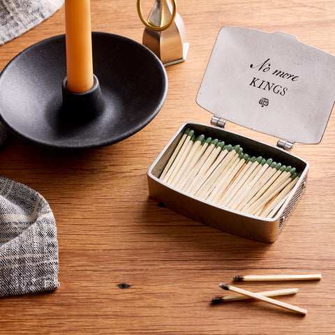 Matchbox with matches on a wooden surface next to a candle and decorative items.