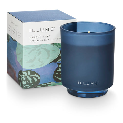 Blue candle with 'ILLUME' branding next to its packaging on a white background