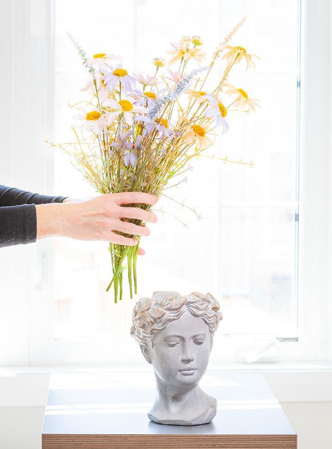 Person arranging flowers into a decorative vase shaped like a face.