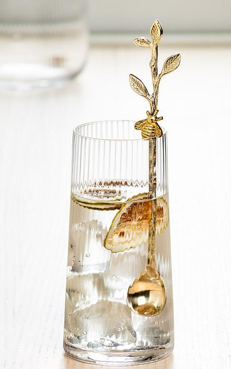 Clear glass with a gold olive branch stirrer on a white background