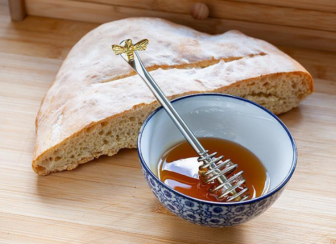 Bread with a bowl of honey and a honey dipper on a wooden surface