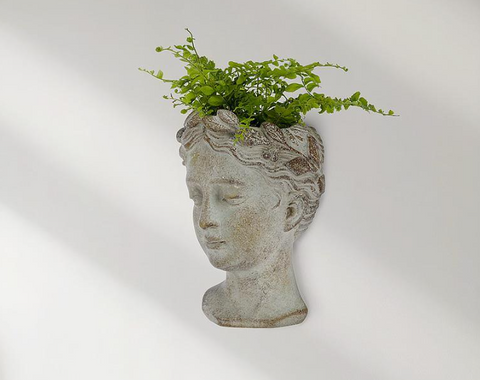Decorative planter shaped like a head with greenery on a white background