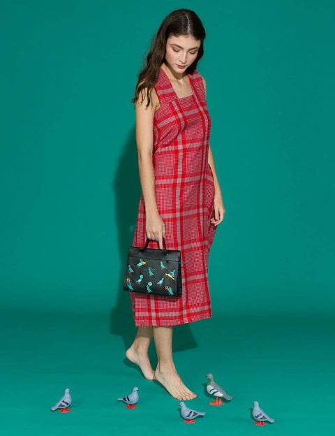 Woman in a red plaid dress holding a black handbag with bird design on a teal background