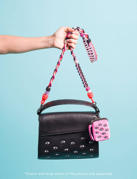 Black handbag with pink and red strap held by a hand against a light blue background