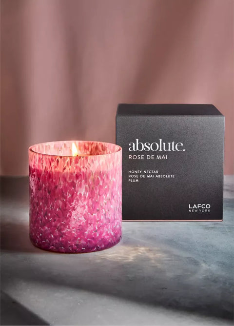 Pink candle with a box labeled 'absolute Rose de Mai' by Lafco on a gray surface.