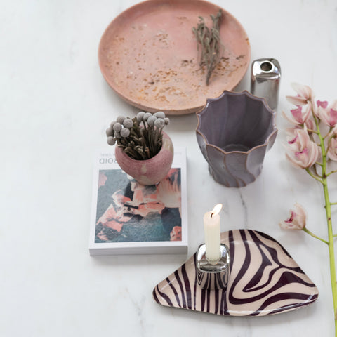 Ceramic items including a plate, vase, and candle holder on a white surface with a book and flowers.