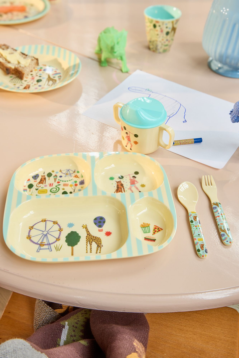 Children's table setting with a plate, cup, and cutlery on a wooden surface.