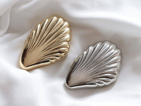 Gold and silver shell-shaped mirror on a white fabric background