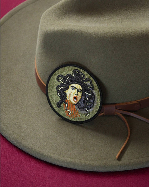 Green hat with embroidered patch on a pink background