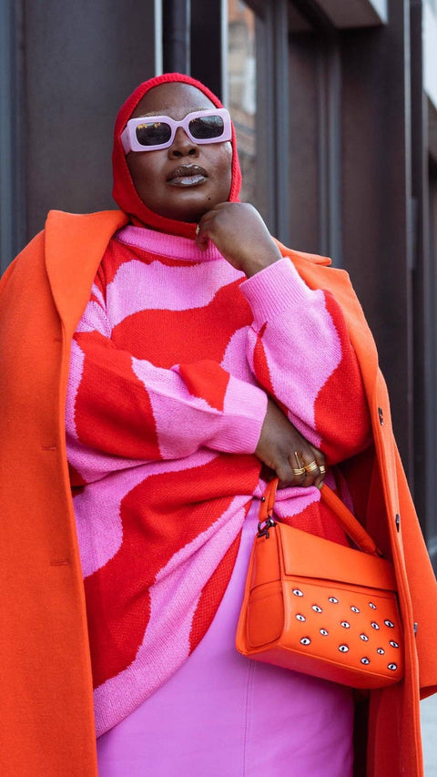 Person wearing a vibrant outfit with a red and pink patterned top, orange coat, and matching bag.