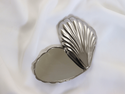 Silver shell-shaped compact mirror on a white fabric background