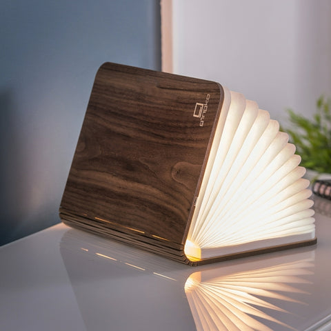 Wooden book-shaped lamp on a reflective surface with a blurred background
