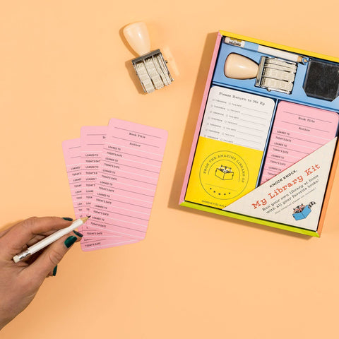 Library card stamping kit with cards, stamps, and instructions on a peach background
