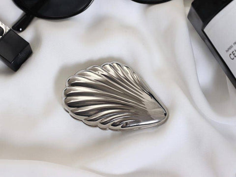 Silver shell-shaped object on a white fabric background