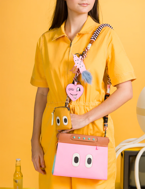 Person wearing a yellow outfit with a colorful bag featuring cartoonish face designs on an orange background.