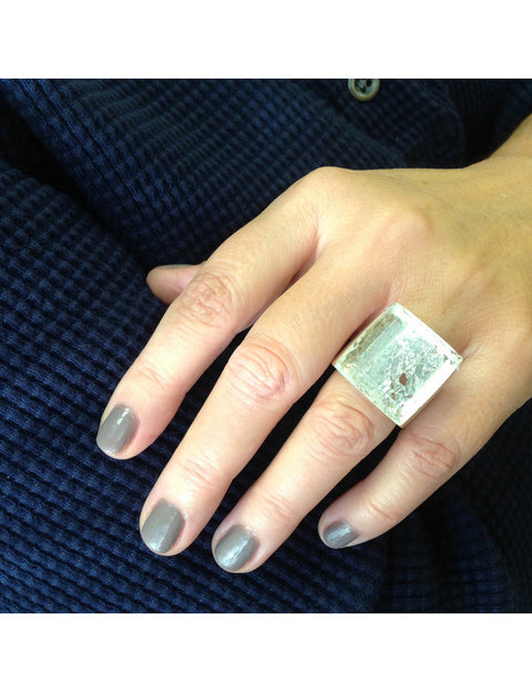 Hand wearing a silver ring with a textured design on a dark textured background