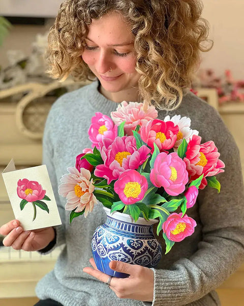Person holding a paper bouquet of pink flowers and a card with a floral design.