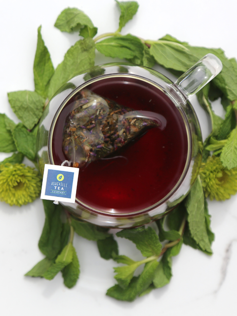 Tea bag steeping in a cup of tea with green leaves and flowers around on a white background